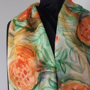 May include: A silk scarf with a hand-painted design of orange and green fruit with leaves. The scarf is a light beige color with a watercolor effect.