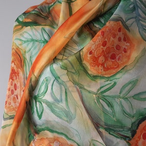 May include: A silk scarf with a watercolor design of orange and red fruit with green leaves on a light background.