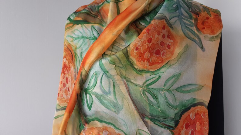 May include: A silk scarf with a watercolor design of orange and red fruit with green leaves on a light background.