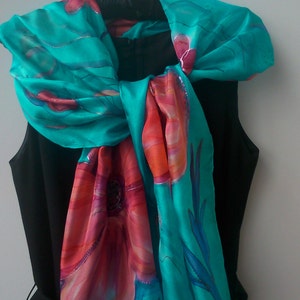May include: A turquoise silk scarf with a floral design in shades of pink, orange, and red. The scarf is tied around the neck of a black sleeveless dress.