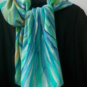 May include: A blue, green, and white silk scarf with a watercolor-like pattern. The scarf is tied around the neck of a black blazer.