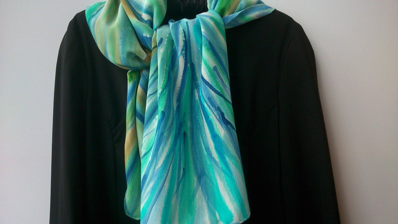 May include: A blue, green, and white silk scarf with a watercolor-like pattern. The scarf is tied around the neck of a black blazer.