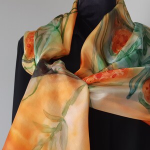 May include: A silk scarf with a hand-painted design of orange and green flowers on a yellow background.