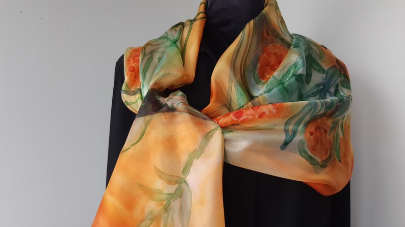 May include: A silk scarf with a hand-painted design of orange and green flowers on a yellow background.