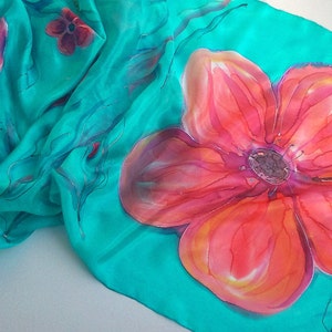May include: A turquoise silk scarf with hand-painted red and orange flowers. The scarf features a floral design with delicate details.