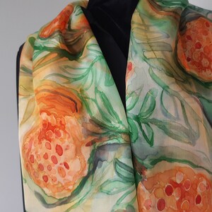 May include: A silk scarf with a watercolor design of orange and green leaves and fruit. The scarf is a light beige color with a subtle sheen.