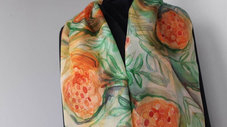 May include: A silk scarf with a watercolor design of orange and green leaves and fruit. The scarf is a light beige color with a subtle sheen.