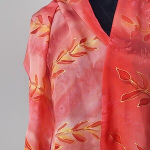 May include: A red silk scarf with a gold leaf design. The scarf is draped over a mannequin.