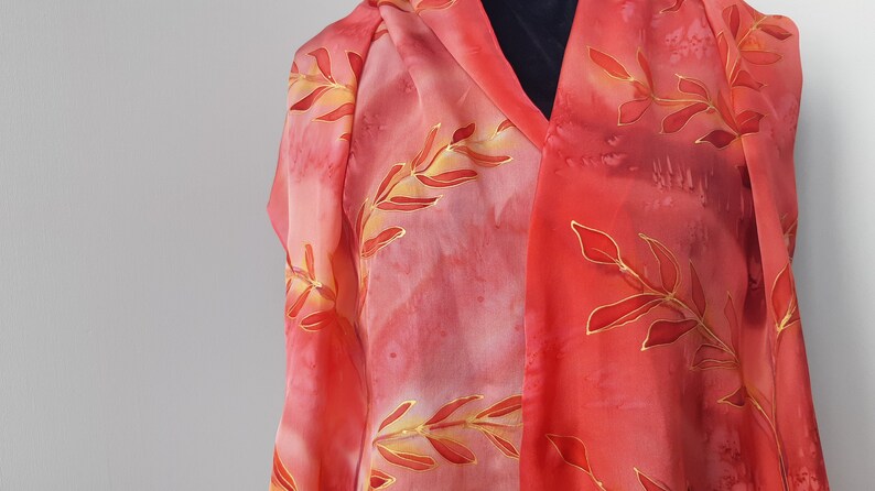 May include: A red silk scarf with a gold leaf design. The scarf is draped over a mannequin.