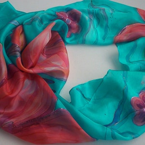 May include: A turquoise silk scarf with a hand-painted design of red and pink flowers. The scarf is folded in half and the design is visible on both sides.