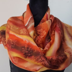 May include: A silk scarf with a hand-painted design in shades of orange, yellow, and brown. The scarf features a flowing, abstract pattern with hints of floral motifs.
