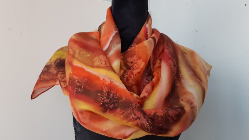 May include: A silk scarf with a hand-painted design in shades of orange, yellow, and brown. The scarf features a flowing, abstract pattern with hints of floral motifs.