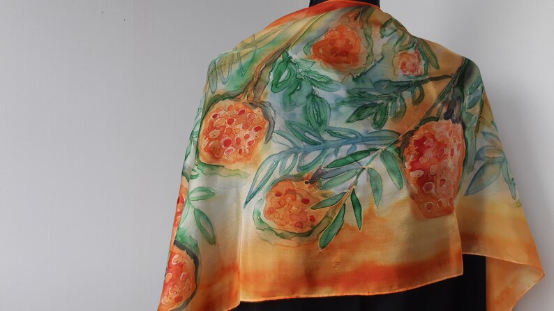 May include: A silk scarf with a watercolor design of orange fruit and green leaves on a yellow and orange background.