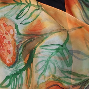 May include: A silk scarf with a watercolor design of orange and green flowers and leaves. The scarf is folded and draped over a person's shoulder.