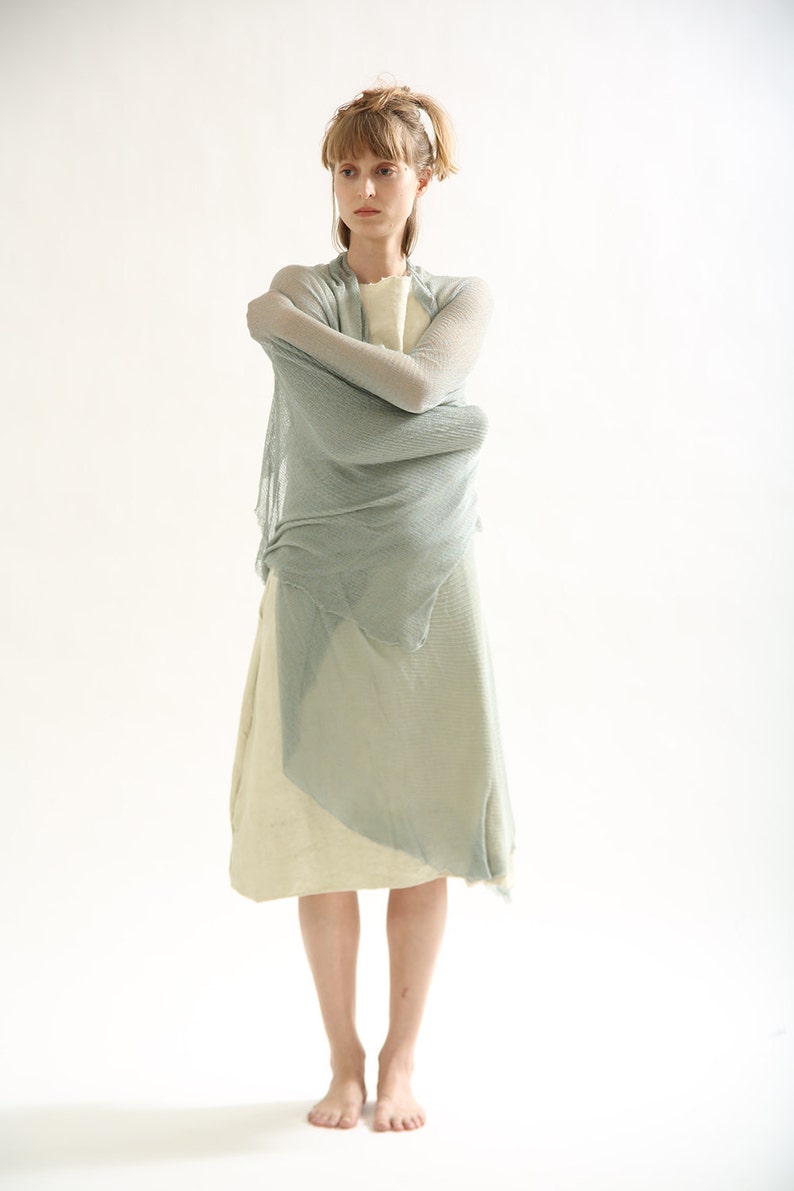 Puede incluir: Una mujer con un vestido de gasa azul claro con una capa interior blanca. El vestido est&aacute; drapeado y fluido, y la mujer est&aacute; de pie con los brazos cruzados.