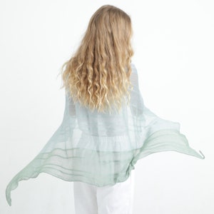 May include: A light blue and green shawl with a flowing design. The shawl is made of a lightweight material and has a gradient effect, transitioning from light blue to green. The shawl is draped over a person's shoulders.