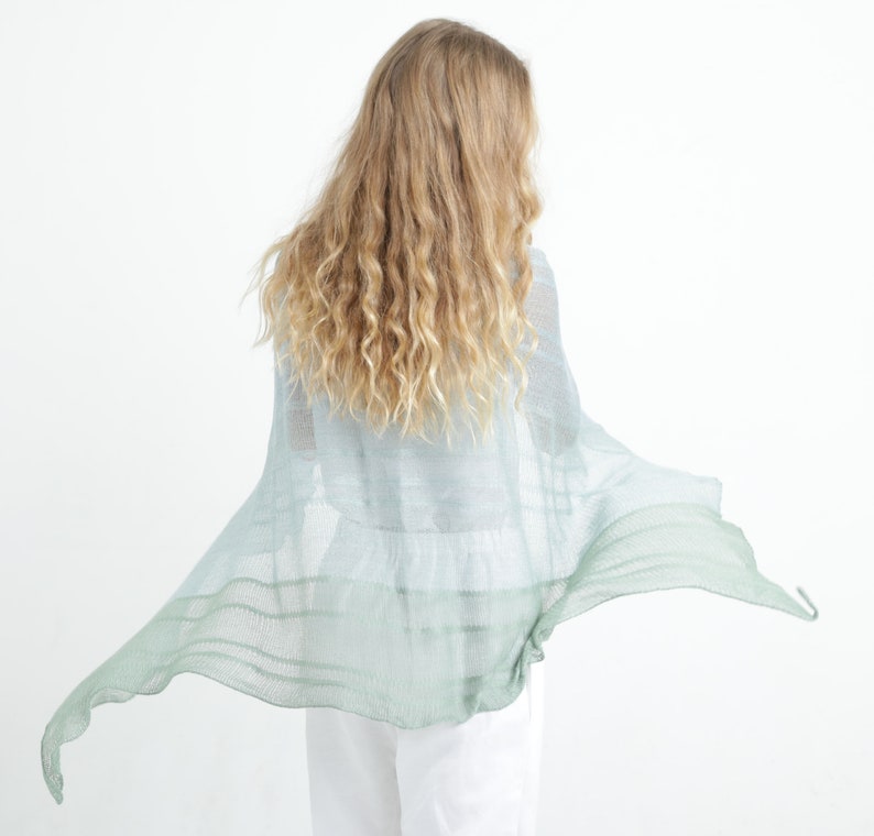 May include: A light blue and green shawl with a flowing design. The shawl is made of a lightweight material and has a gradient effect, transitioning from light blue to green. The shawl is draped over a person's shoulders.