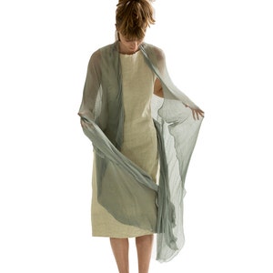 Puede incluir: Una persona lleva una estola de gasa verde claro sobre un vestido beige. La estola est&aacute; drapeada sobre los hombros de la persona y ondea con el viento.