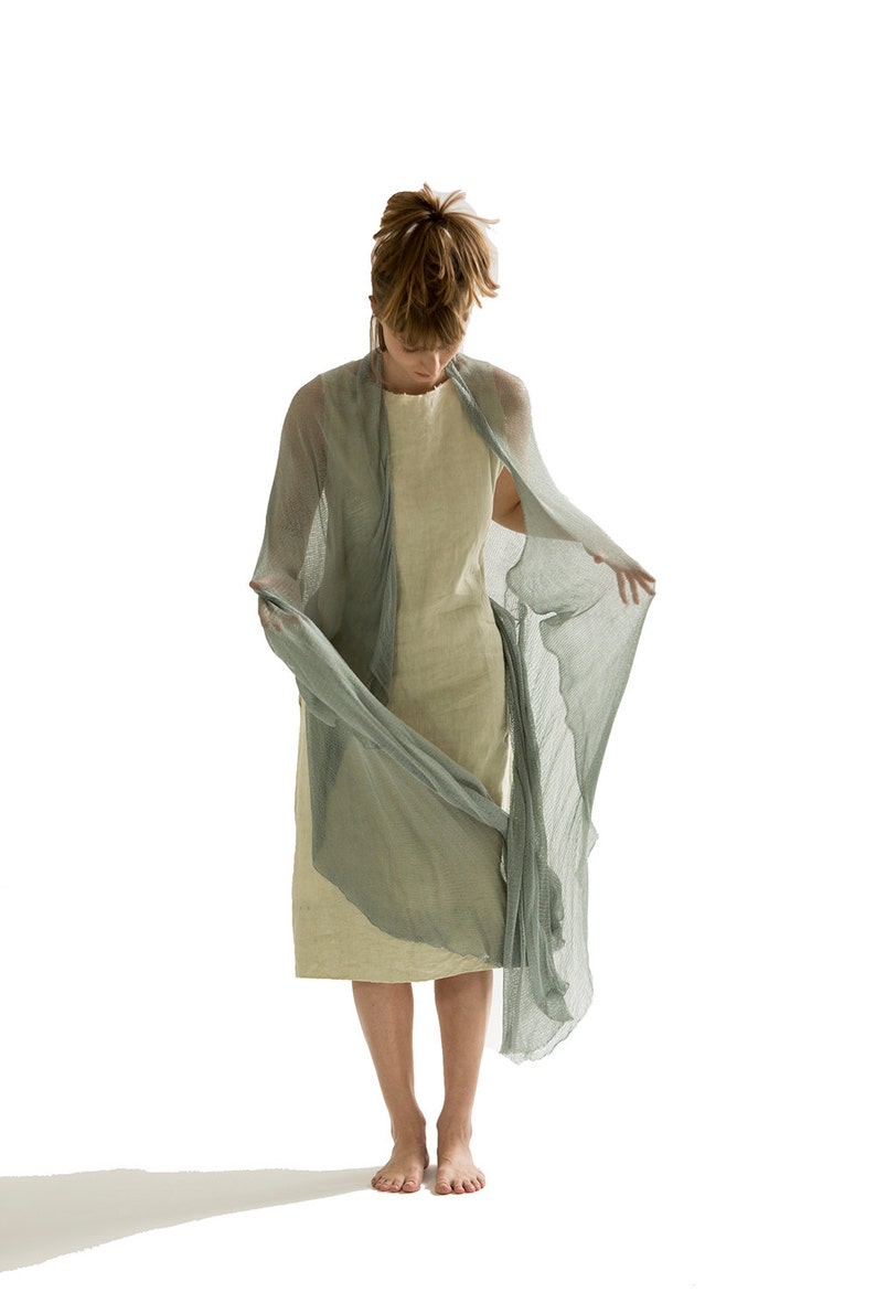 Puede incluir: Una persona lleva una estola de gasa verde claro sobre un vestido beige. La estola est&aacute; drapeada sobre los hombros de la persona y ondea con el viento.