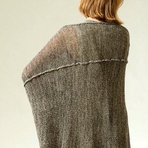 Puede incluir: Un c&aacute;rdigan de punto gris con un tejido suelto y abierto. El c&aacute;rdigan se muestra desde la parte posterior y tiene un ajuste holgado.