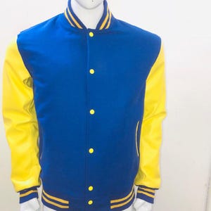 Può includere: Una giacca varsity con corpo blu reale e maniche giallo brillante. La giacca presenta un colletto alla coreana, bottoni a pressione gialli sul davanti e bordi a coste a righe gialle e blu sul colletto, sui polsini e sull'orlo inferiore.