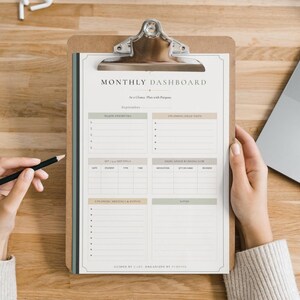 May include: A monthly dashboard planner sheet on a brown clipboard with a silver metal clip. The white paper features sections for major priorities, to-do lists, meetings, inventory, and notes, with the text Monthly Dashboard and September.