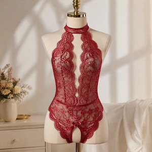 May include: A deep red lace bodysuit featuring a high halter neckline with a cutout design, intricate floral patterns throughout the fabric, and a small satin bow detail at the center of the leg opening, displayed on a mannequin torso.