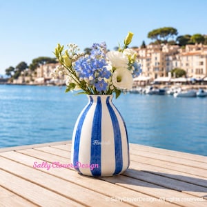 May include: A ceramic vase with vertical blue and white stripes containing a bouquet of white and blue flowers. The word Flourish is printed on the front of the vase, and the text Sally Clover Design appears in pink script on the lower left.