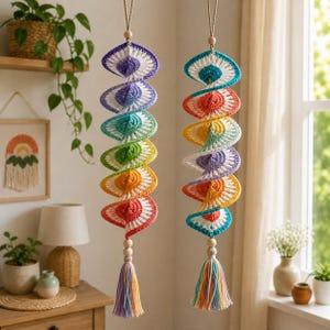 Puede incluir: Dos decoraciones colgantes en espiral hechas de hilo de ganchillo con un degradado de colores arcoíris. Cada pieza presenta una serie de segmentos circulares conectados en violeta, azul, verde, amarillo, naranja y rojo, con una cuenta de madera.