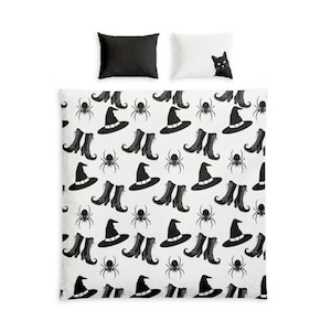 Puede incluir: Un juego de cama que incluye una funda nórdica blanca con un patrón repetitivo negro de sombreros de bruja, botas con cordones y arañas. El conjunto incluye dos fundas de almohada: una negra lisa y una blanca con un gato negro en la esquina.