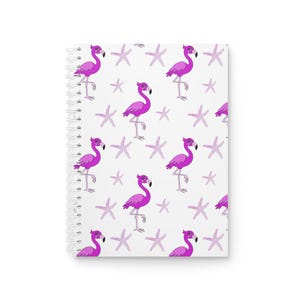 Puede incluir: Un cuaderno de espiral con un patrón repetitivo de flamencos de color rosa brillante y estrellas de mar de color morado claro sobre un fondo blanco. El cuaderno tiene una encuadernación de espiral metálica blanca en el lado izquierdo.