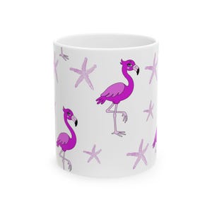 Puede incluir: Una taza de cerámica blanca con un patrón repetitivo de flamencos de color rosa brillante y estrellas de mar de color morado claro. Los flamencos están representados en estilo caricatura con cuellos largos, patas finas y marcas de corazón.