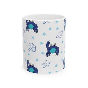 Puede incluir: Una taza de cerámica blanca con un patrón repetitivo de cangrejos azul oscuro con vientres azul claro, estrellas de cuatro puntas azul claro y conchas marinas dibujadas con líneas azules. El diseño cubre la superficie exterior de la taza.