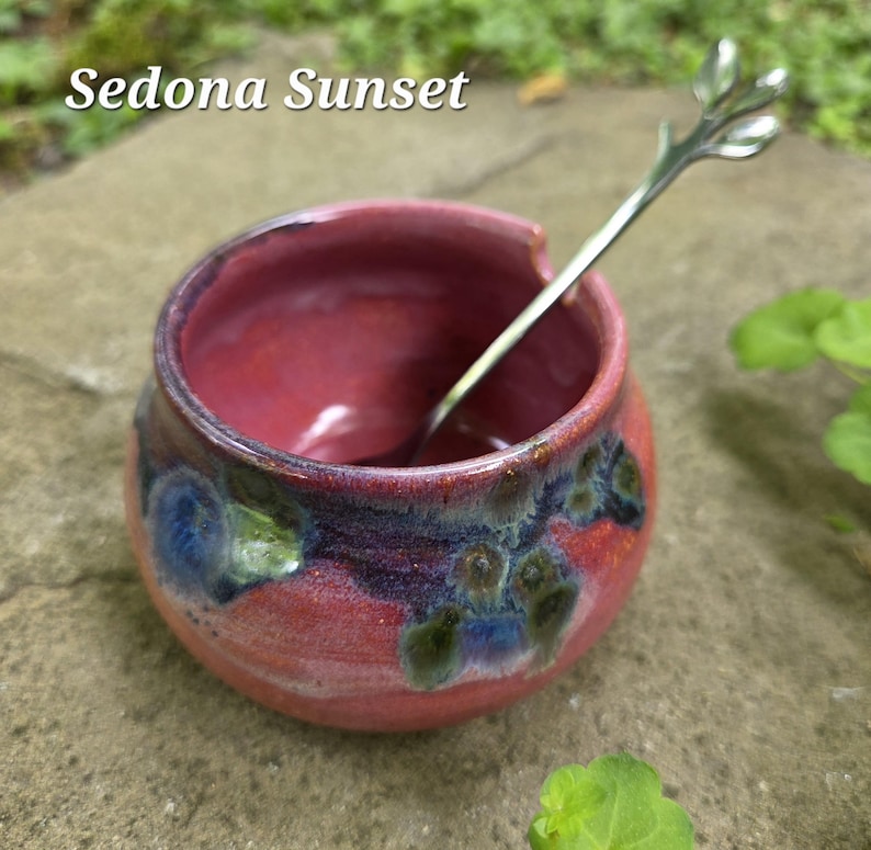 May include: A small, round, red ceramic bowl with a silver spoon. The bowl has a textured surface with blue and green accents. The text "Sedona Sunset" is at the top.