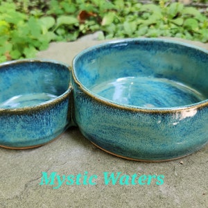 May include: A teal blue ceramic double bowl with a smaller bowl attached to the side. The bowls have a dark brown rim and a speckled glaze.