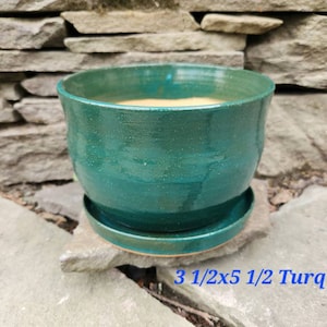 May include: A turquoise ceramic planter with a saucer, measuring 3 1/2 inches by 5 1/2 inches.