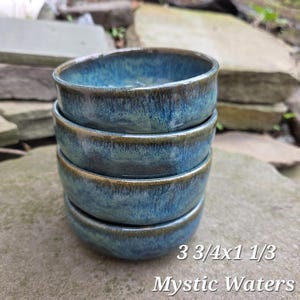May include: A stack of four small, round ceramic bowls with a glossy, blue glaze and a dark brown rim. The bowls are approximately 3.75 inches in diameter and 1.33 inches tall. The text "Mystic Waters" is at the bottom.