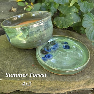 May include: A ceramic bowl and matching saucer featuring a glossy green glaze with blue circular accents. The text Summer Forest 4x2 is printed on the image. The bowl has a rounded shape and the saucer is flat with a raised edge, both showing variations in color intensity across their surfaces.