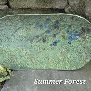 May include: An oval ceramic tray featuring a textured surface with a repeating wave-like pattern in shades of sage green and olive. The glaze includes patches of deep blue and dark brown accents. The text Summer Forest is printed at the bottom.