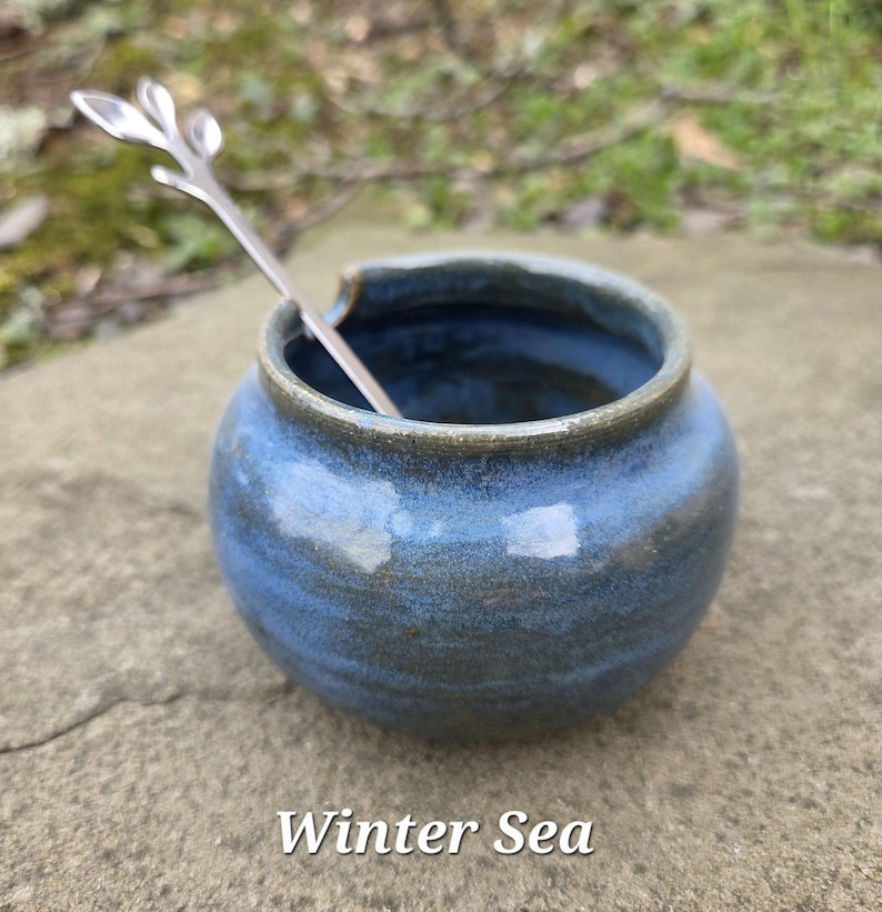 May include: A small, round, blue ceramic jar with a silver spoon inside. The jar has a dark blue rim and a glossy finish. The text "Winter Sea" is at the bottom of the image.
