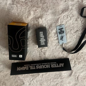 May include: A black and yellow rectangular box with white text, a small black box with white text, a light blue rectangular tag with black text and a black lanyard, and a long black rectangular sign with white text reading AFTER HOURS TIL DAWN.