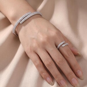 May include: A silver-toned bypass bracelet and a matching bypass ring, both featuring a pavé-style setting with numerous small, clear, sparkling stones covering the entire outer surface of the metal bands in a continuous, shimmering design.
