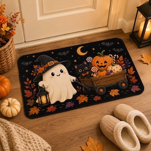 May include: A rectangular doormat featuring a black background with a white ghost wearing a witch hat and holding a lantern. A black cat sits in a wooden wagon filled with pumpkins, lollipops, and autumn leaves under a crescent moon and bats.