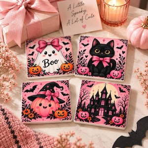 Könnte beinhalten: Vier quadratische Keramikuntersetzer mit Halloween-Illustrationen in Pink und Schwarz. Die Motive zeigen ein Gespenst mit rosa Schleife, eine schwarze Katze mit rosa Schleife, einen Kürbis mit Hexenhut und ein Spukschloss mit Fledermäusen.