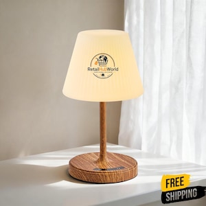 Puede incluir: Una lámpara de mesa con base de imitación madera y pantalla acampanada de color blanco roto. La pantalla presenta un logotipo circular con el texto RetailHubWorld. La base tiene un tallo cilíndrico liso y una parte inferior redonda y plana.