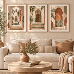 Peut inclure: Un ensemble de trois cadres muraux représentant des scènes architecturales avec des portes en arc, des murs en terre cuite, des carreaux verts à motifs et des palmiers en pot. Les cadres en bois clair sont disposés au-dessus d'un canapé beige.