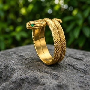 Könnte beinhalten: Ein goldfarbener Ring in Form einer gewundenen Schlange mit einer strukturierten, schuppenartigen Oberfläche. Der Schlangenkopf ist mit einem kleinen, leuchtend grünen Edelstein als Auge besetzt. Das Band windet sich um sich selbst.
