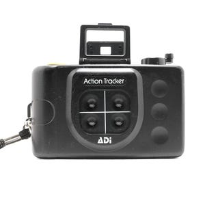 May include: A black ADi Action Tracker film camera featuring four lenses arranged in a square grid on the front. The camera has a pop-up viewfinder, a black wrist strap attached to the side, and three circular indentations on the right side.
