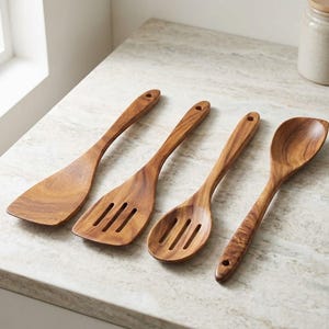 May include: A set of four wooden kitchen utensils featuring a solid turner, a slotted turner, a slotted spoon, and a solid spoon. Each utensil is crafted from brown wood with a visible grain pattern and includes a small hole at the end of the handle.