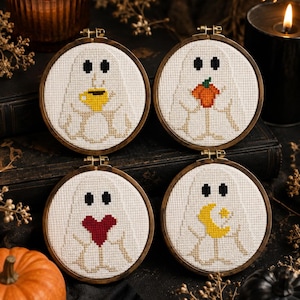 以下が含まれることがあります： 白い布に白い幽霊のクロスステッチが施された、4つの円形木製刺繍枠。それぞれの幽霊は、黄色いコーヒーマグ、オレンジ色のカボチャ、赤いハート、星付きの黄色い三日月という異なるアイテムを持っています。